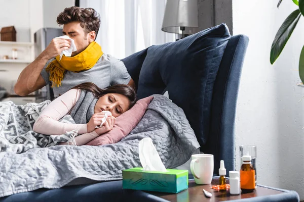 Sick girlfriend and handsome boyfriend sneezing and holding napkins — Stock Photo