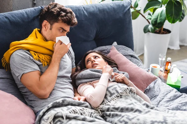 Sick girlfriend and handsome boyfriend sneezing and holding napkins — Stock Photo