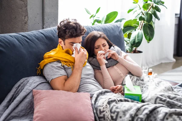 Sick girlfriend and boyfriend sneezing and holding napkins in apartment — Stock Photo