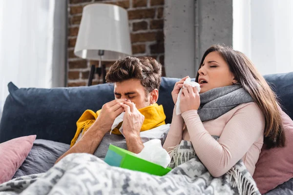 Novia enferma y novio estornudando y sosteniendo servilletas en el apartamento - foto de stock