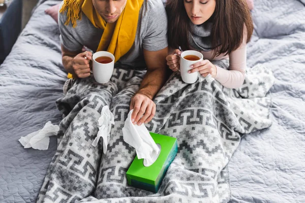 Cropped view of sick girlfriend and boyfriend holding cups and taking napkin — Stock Photo