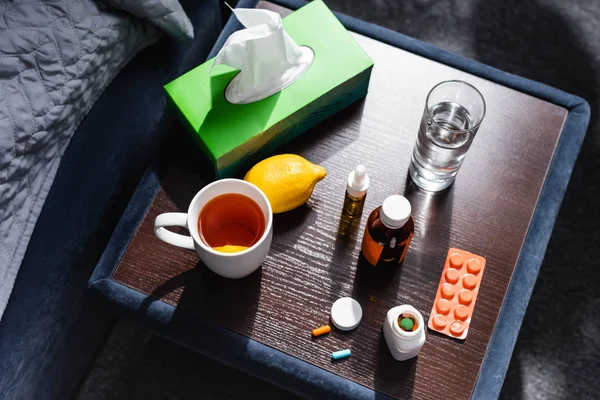 Vue de dessus de la table de chevet avec tasse, verre d'eau, citron, serviettes et médicaments — Photo de stock