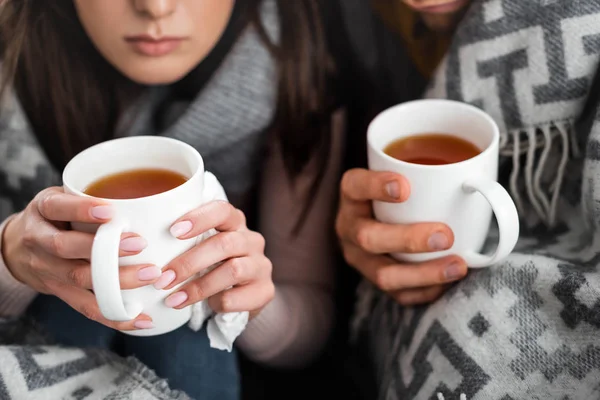 Vista ritagliata di fidanzata malata e fidanzato coperto con coperta che tiene tazze di tè — Foto stock
