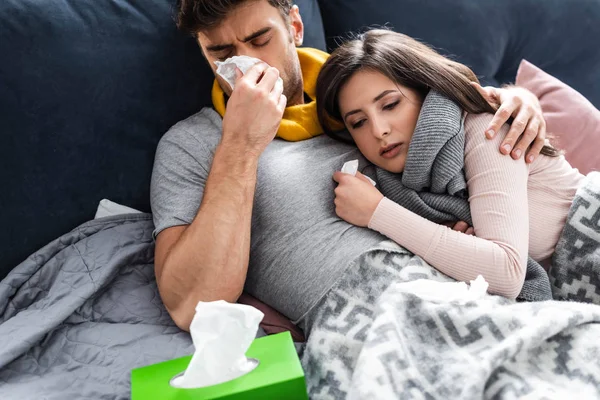 Sick girlfriend and boyfriend sneezing and lying in bed — Stock Photo