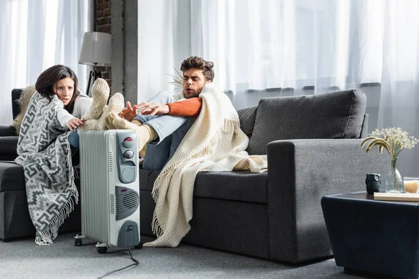 Attractive girlfriend and boyfriend covered with blankest warming up near heater — Stock Photo