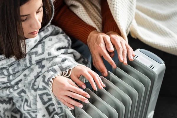 Cropped view of girlfriend and boyfriend covered with blankest warming up near heater — Stock Photo