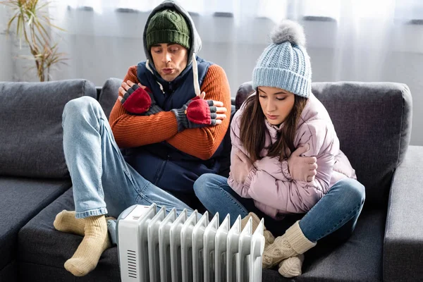 Attractive girlfriend and boyfriend in winter outfit warming up near heater — Stock Photo