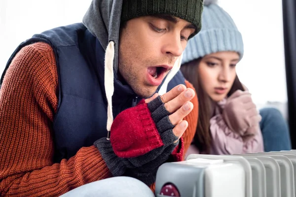 Selective focus of girlfriend and boyfriend in winter outfit warming up near heater — Stock Photo