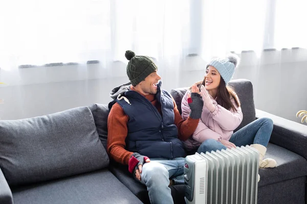 Attraktive Freundin und Freund im Winteroutfit wärmen sich in der Nähe der Heizung auf und geben High Five — Stockfoto