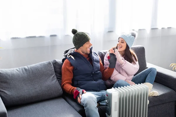 Attractive girlfriend and boyfriend in winter outfit warming up near heater and giving high five — Stock Photo