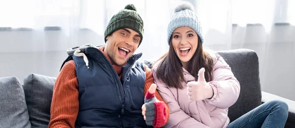 Панорамный снимок девушки и парня в зимнем наряде, улыбающихся и показывающих большие пальцы вверх — стоковое фото