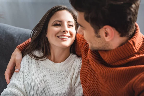 Atractiva novia y novio en suéteres sonriendo y abrazándose en el apartamento - foto de stock