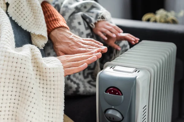 Cropped view of girlfriend and boyfriend covered with blankest warming up near heater — Stock Photo