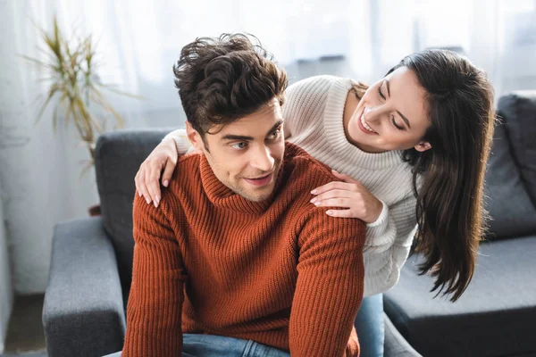 Привлекательная девушка и парень в свитерах улыбаются и обнимаются в квартире — стоковое фото