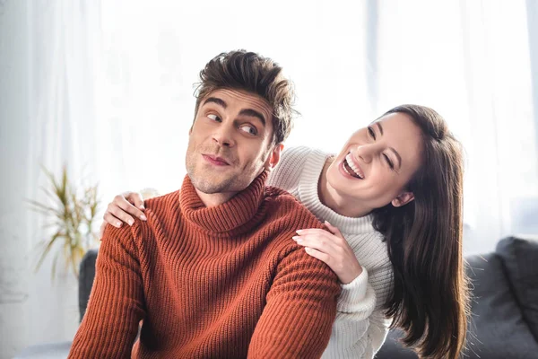 Atractiva novia y novio en suéteres sonriendo y abrazándose en el apartamento - foto de stock