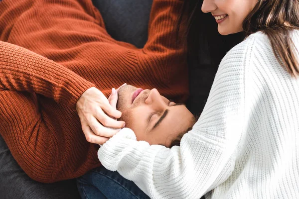 Boyfriend lying on knees of girlfriend in sweater and smiling in apartment — Stock Photo