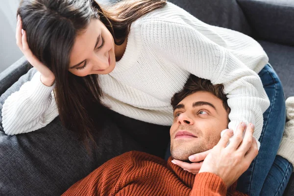 Boyfriend lying on knees of attractive girlfriend in sweater and smiling in apartment — Stock Photo