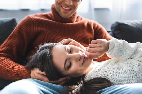 Foco selectivo de novia atractiva en suéter sonriendo y acostado en las rodillas del novio - foto de stock