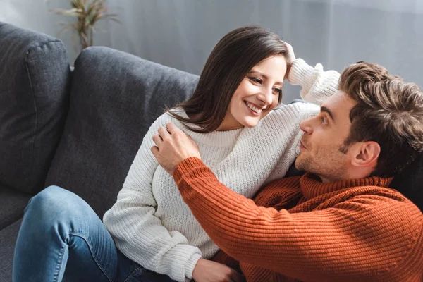 Attractive girlfriend in sweater and handsome boyfriend hugging and sitting on sofa — Stock Photo