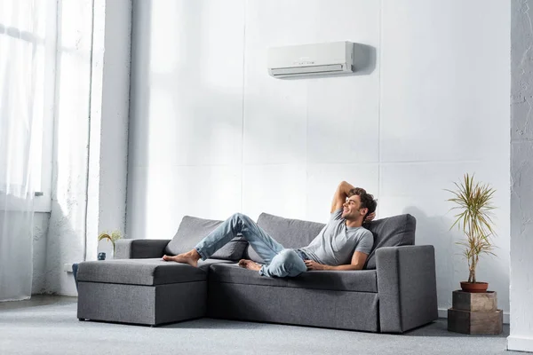 Handsome and smiling man in jeans and t-shirt lying on sofa — Stock Photo