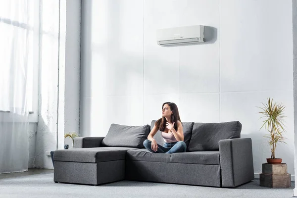 Attractive and shocked woman sitting on sofa and looking away — Stock Photo