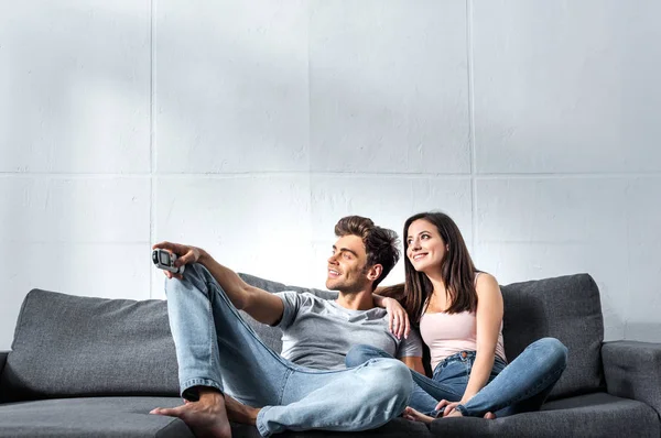 Attraktive Freundin und schöner Freund mit Fernbedienung auf dem Sofa sitzend — Stockfoto