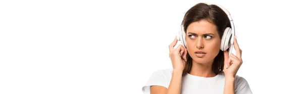 Mujer joven atractiva confundida escuchando música con auriculares, aislado en blanco - foto de stock