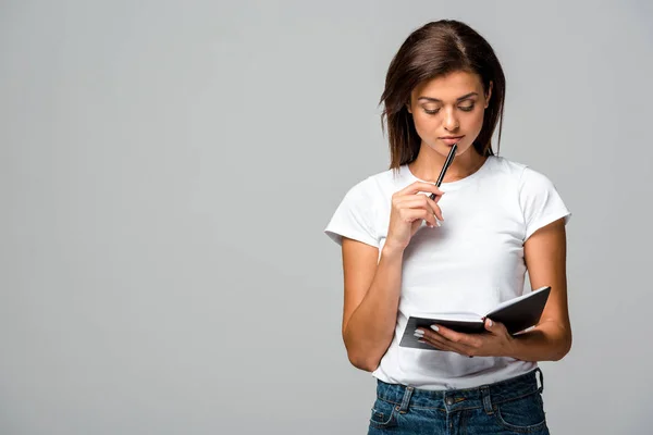 Nachdenkliche junge Frau mit Stift und Notizbuch, isoliert auf grau — Stockfoto