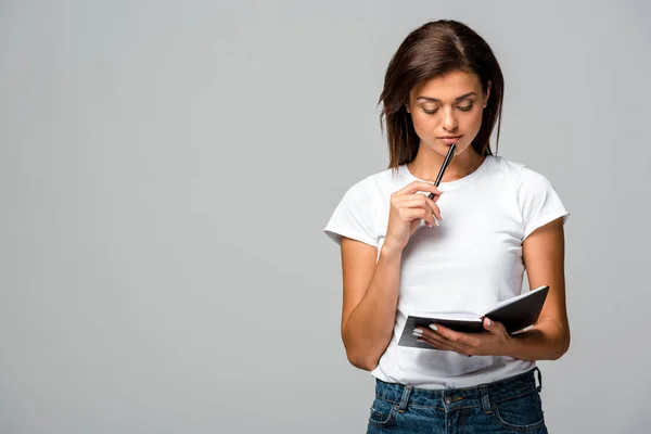 Pensive young woman holding pen and notebook, isolated on grey — Stock Photo