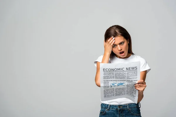 Bela mulher chocada lendo jornal econômico, isolado em cinza — Fotografia de Stock