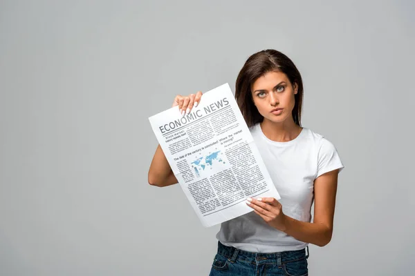 Serious young woman showing economic newspaper, isolated on grey — Stock Photo