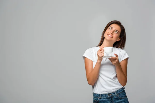 Sognante ragazza sorridente in possesso di una tazza di caffè, isolato su grigio — Foto stock