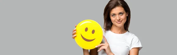 KYIV, UCRANIA - 10 DE SEPTIEMBRE DE 2019: mujer hermosa feliz sosteniendo emoji sonriente amarillo, aislado en gris - foto de stock