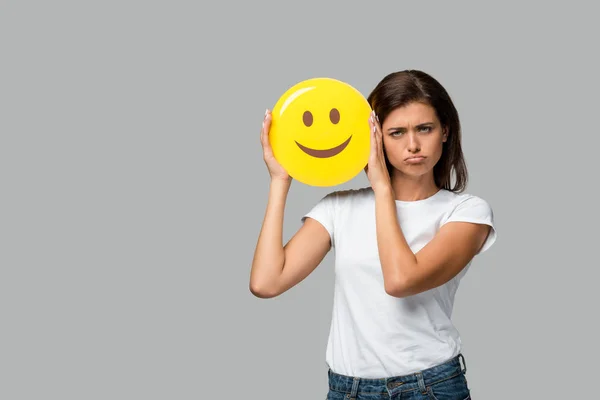 KYIV, UCRANIA - 10 DE SEPTIEMBRE DE 2019: mujer molesta sosteniendo emoji sonriente amarillo, aislada en gris - foto de stock