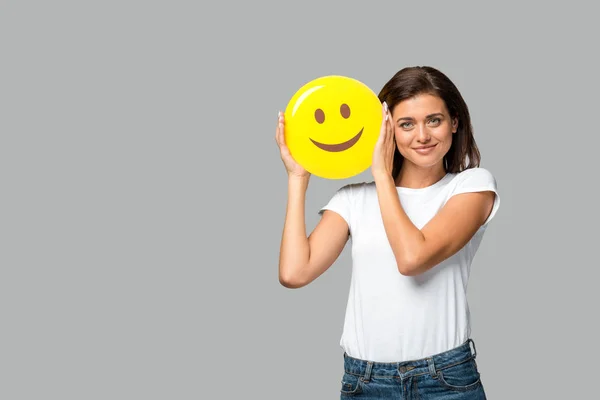 KYIV, UCRANIA - 10 DE SEPTIEMBRE DE 2019: joven feliz sosteniendo emoji sonriente amarillo, aislado en gris - foto de stock