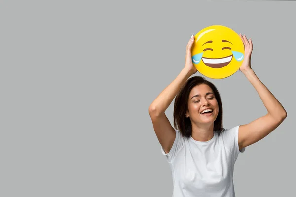 KYIV, UCRANIA - 10 DE SEPTIEMBRE DE 2019: mujer alegre sosteniendo emoji amarillo riéndose, aislado en gris - foto de stock