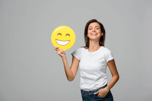 KYIV, UCRANIA - 10 DE SEPTIEMBRE DE 2019: mujer alegre sosteniendo emoji sonriente feliz amarillo, aislado en gris - foto de stock