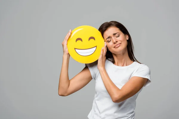 KYIV, UCRANIA - 10 DE SEPTIEMBRE DE 2019: chica emocional sosteniendo emoji sonriente feliz amarillo, aislado en gris - foto de stock