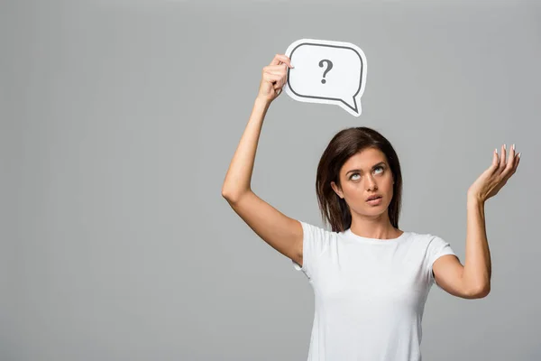 Confused woman thinking and holding speech bubble with question mark, isolated on grey — Stock Photo