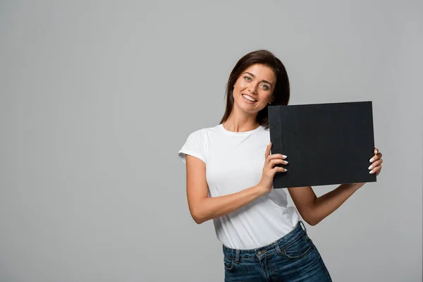 Hermosa mujer feliz sosteniendo tablero negro vacío, aislado en gris - foto de stock