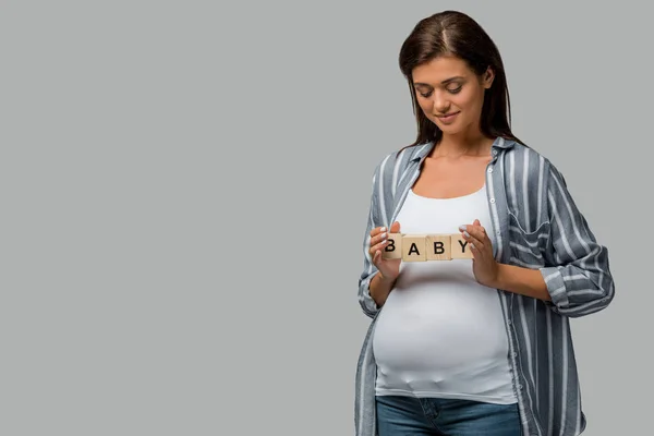 Beautiful happy pregnant woman holding alphabet blocks with baby sign, isolated on grey — Stock Photo