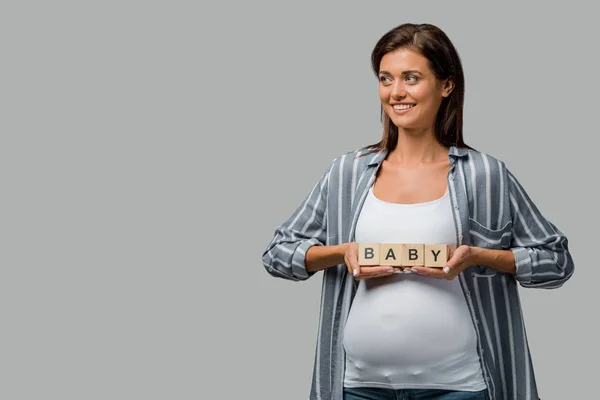 Cheerful pregnant woman holding alphabet cubes with baby sign, isolated on grey — Stock Photo