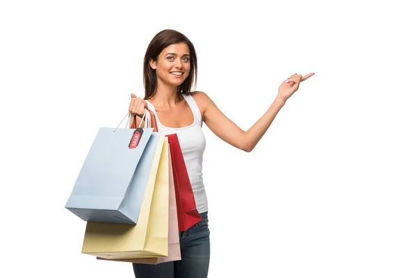 Sonriente chica sosteniendo bolsas de compras con venta signos mientras señala aislado en blanco - foto de stock