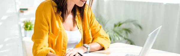 Vista recortada del freelancer femenino que trabaja en el ordenador portátil y la escritura en la oficina en casa - foto de stock