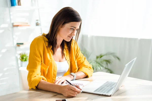 Hermosa freelancer trabajando en el ordenador portátil y la escritura en la oficina en casa - foto de stock