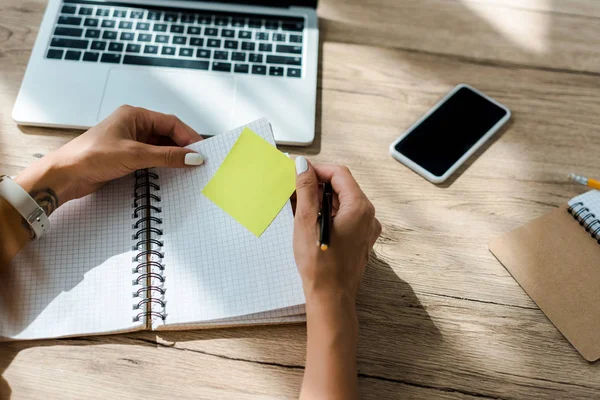 Cropped view of freelancer working with notebook, sticker, laptop and smartphone on table — Stock Photo