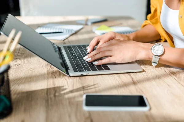 Vista recortada del freelancer que trabaja con el ordenador portátil y el smartphone en la mesa - foto de stock