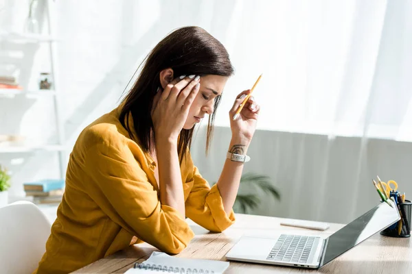 Freelance fatigué ayant mal à la tête tout en travaillant sur ordinateur portable au bureau à domicile — Photo de stock