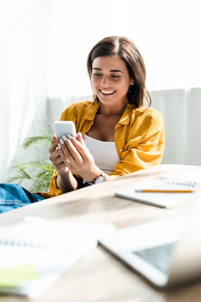 Hermosa freelancer alegre usando teléfono inteligente en la oficina en casa — Stock Photo