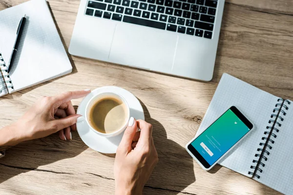 KYIV, UCRANIA - 10 de septiembre de 2019: vista recortada del freelancer con taza de café, laptop y smartphone con aplicación de twitter - foto de stock